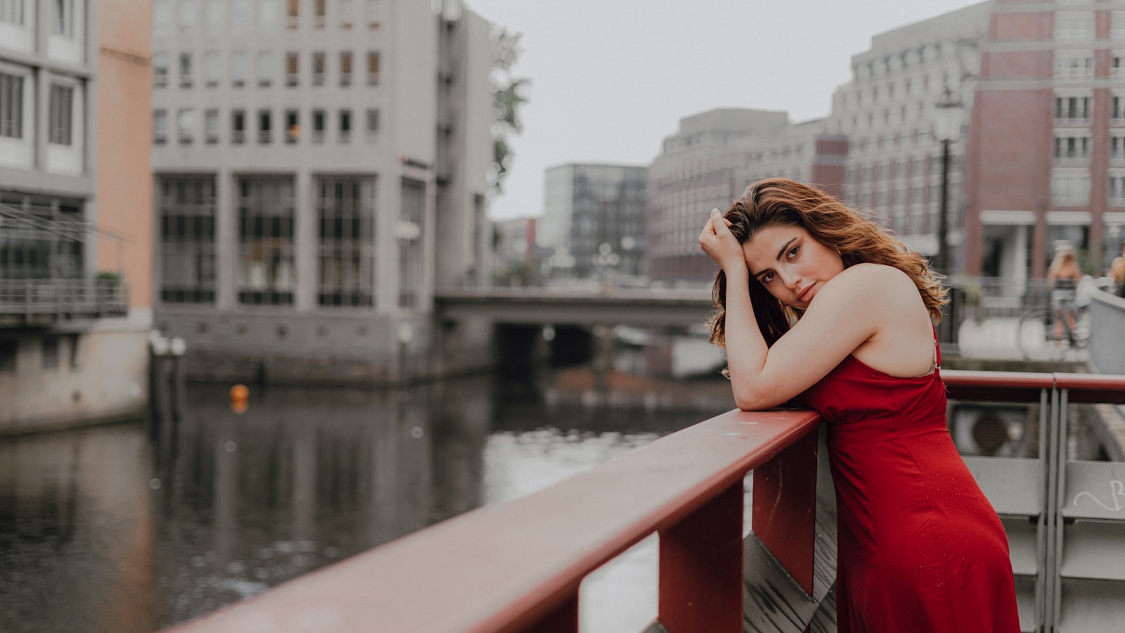 Photo by Khaled Ali woman in red sleeveless dress sitting on brown wooden bench near body of water during daytime